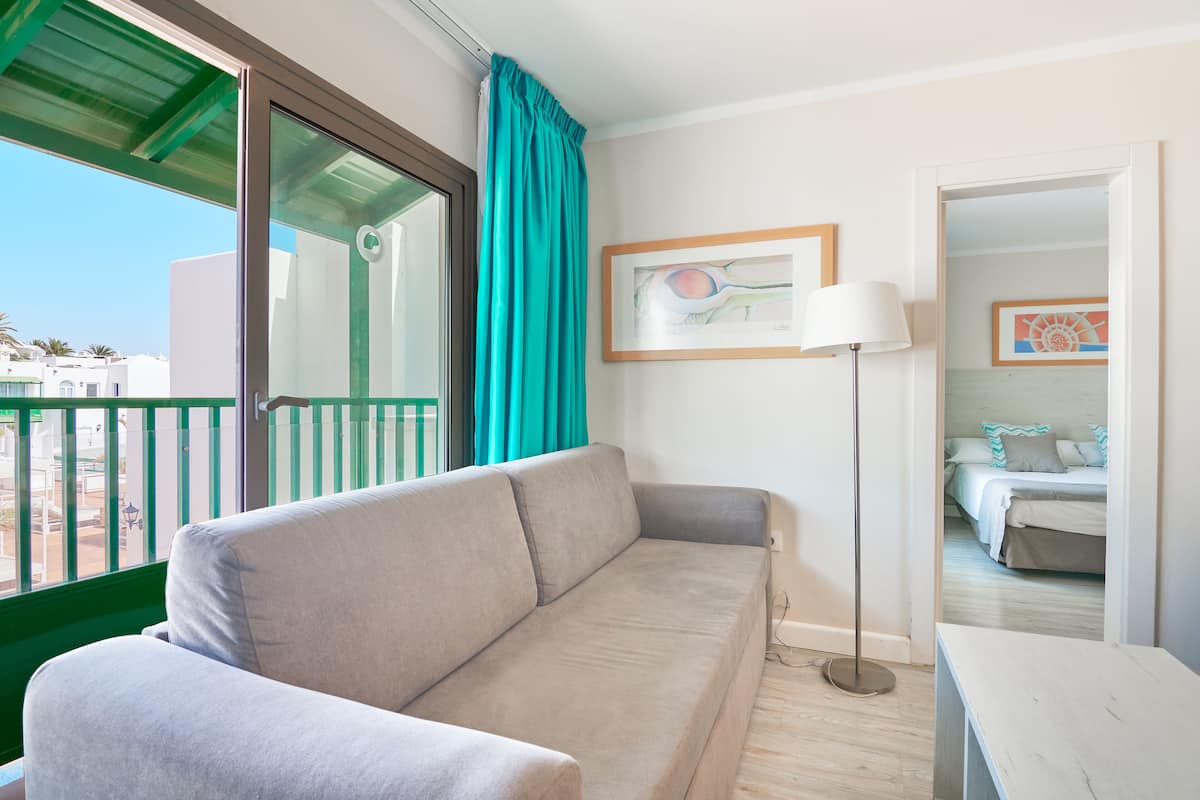 A modern room with a grey sofa, a floor lamp, and a view of a balcony.