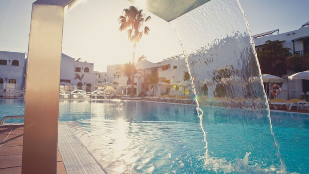 A swimming pool with a water feature, palm trees, and a clear sky. - Gloria Izaro Club Hotel (Tías)