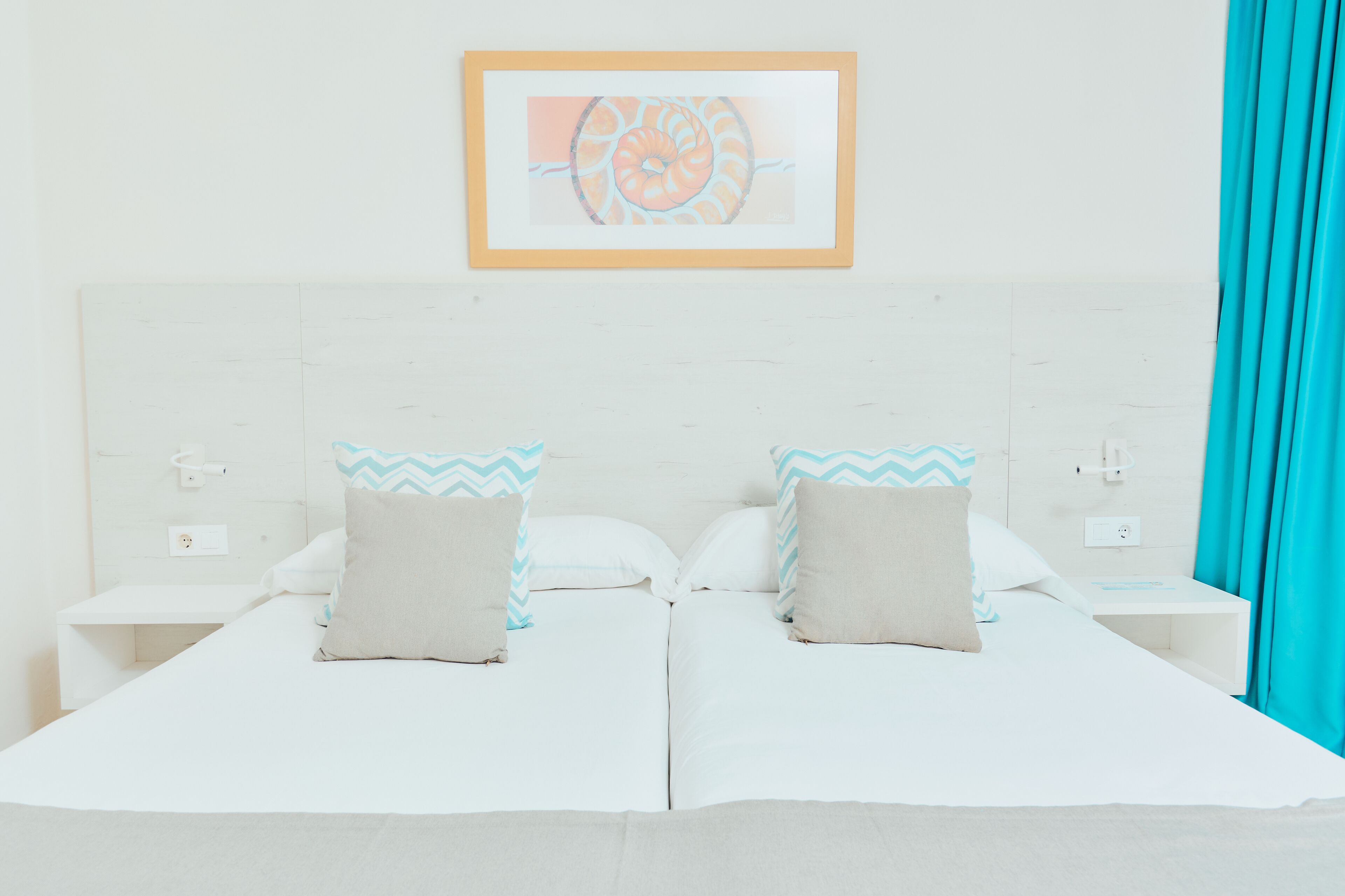 Una cama doble con dos almohadas, una mesita de noche con un teléfono y un cuadro enmarcado en la pared.