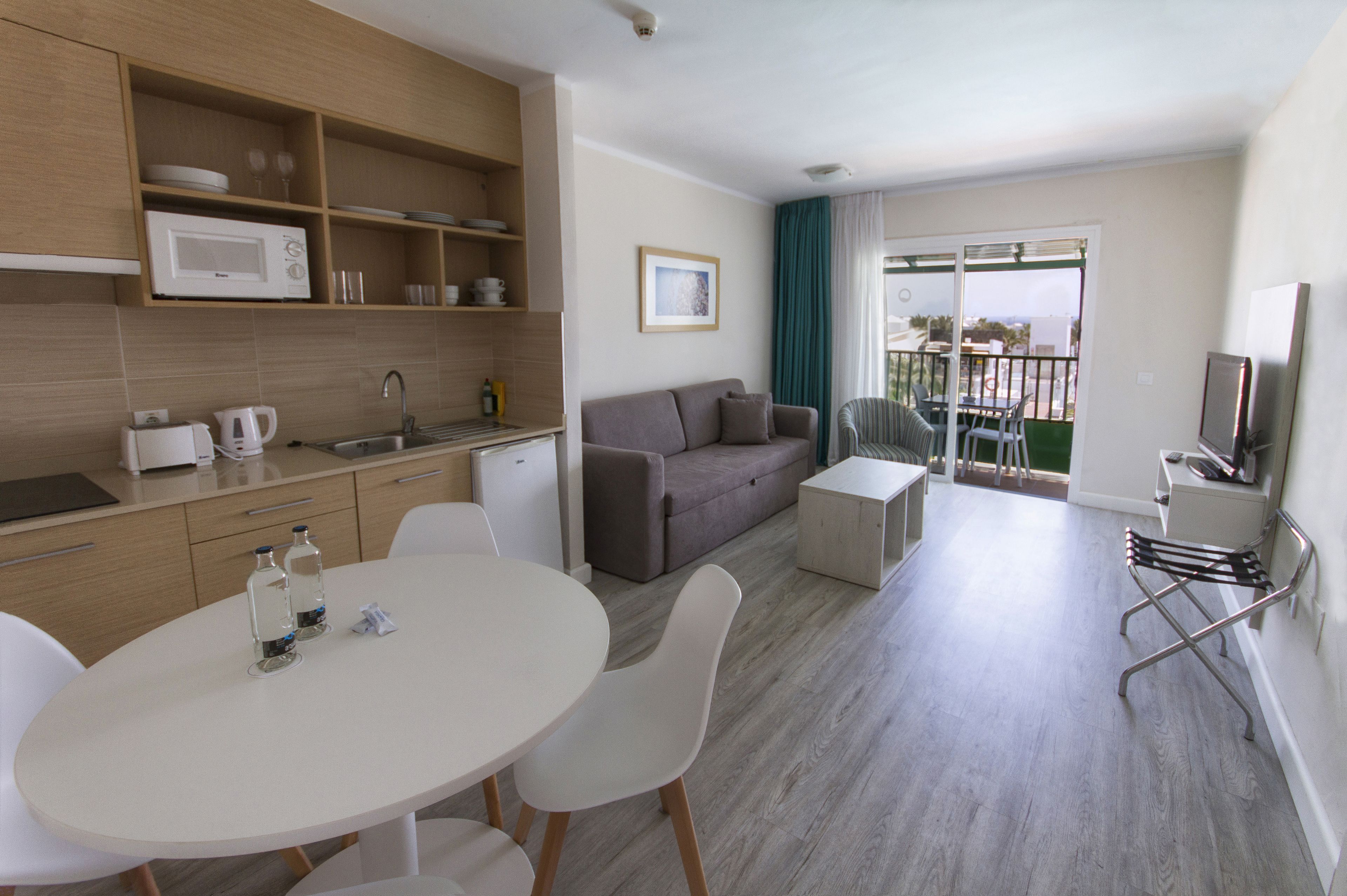 Een moderne woonkamer met een bank, een eettafel met stoelen, een keuken met een magnetron, en een balkon met uitzicht.