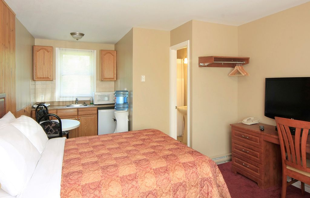 A hotel room with a bed, a desk, a television, a water dispenser, and a small kitchenette.