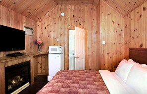 Una habitación de cabaña de madera con una cama, chimenea, televisión y microondas.