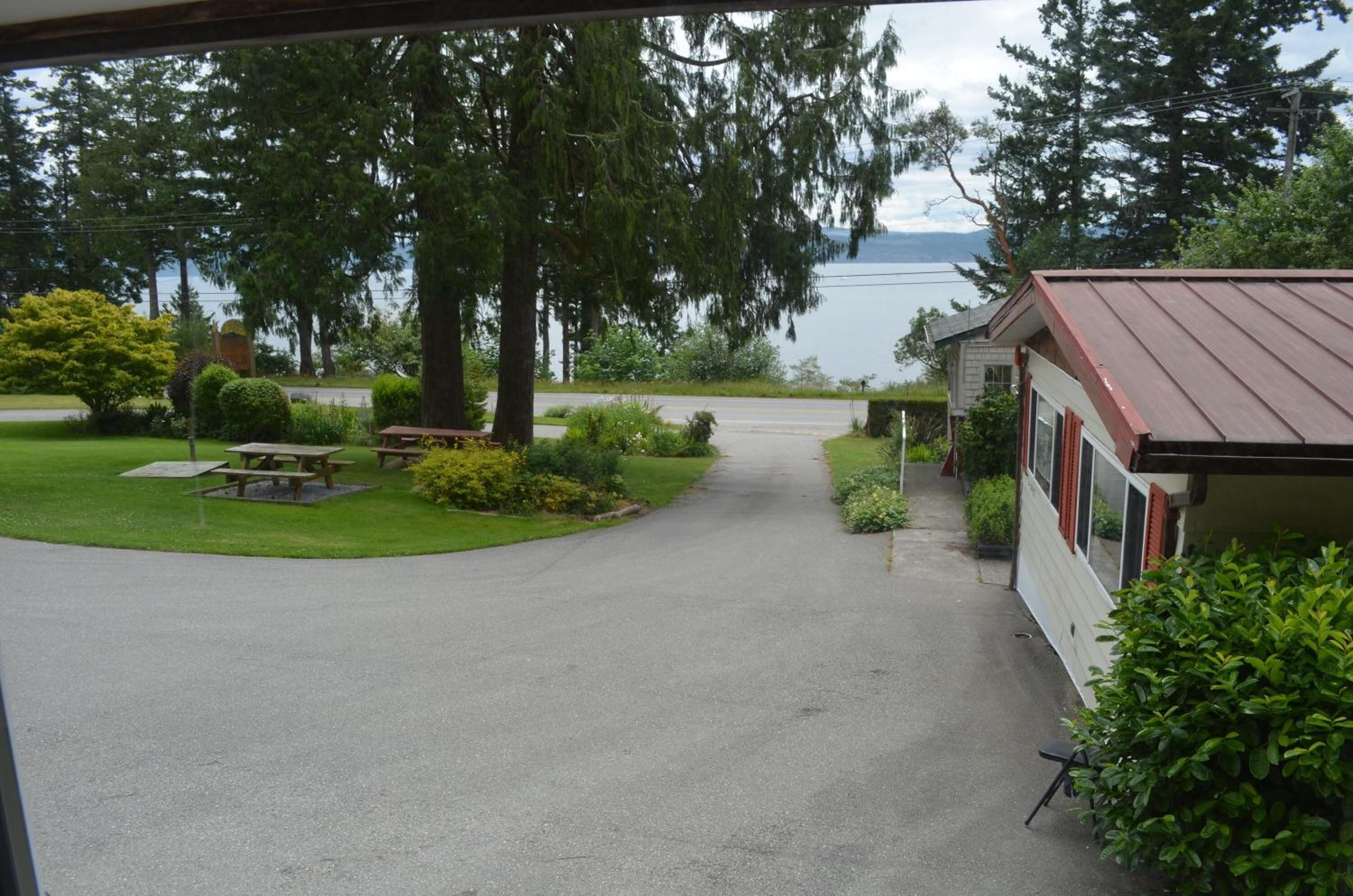 A lakeside lodge with a paved driveway leading to a building with a red roof.
