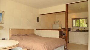 Een slaapkamer met een bed, nachtkastje en uitzicht op de keuken.