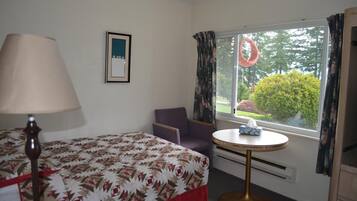 A hotel room with a bed, a chair, a small table with a tissue box, a lamp, and a window with curtains.