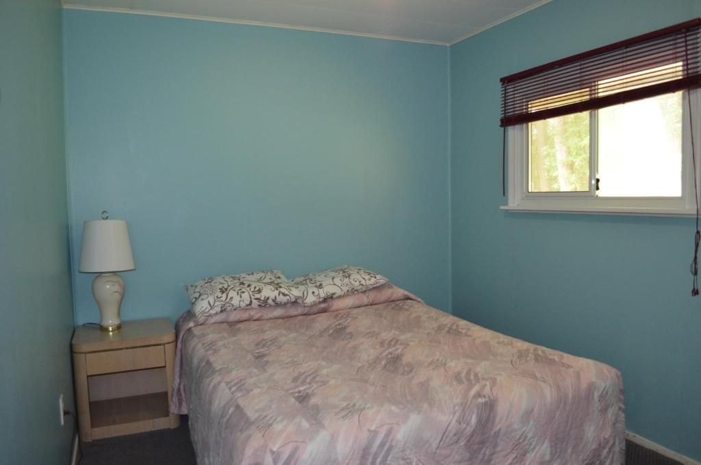 A bedroom with a bed, a nightstand with a lamp, and a window with blinds.