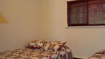 A bedroom with two beds, each with patterned bedding. There is a window with blinds on the wall.