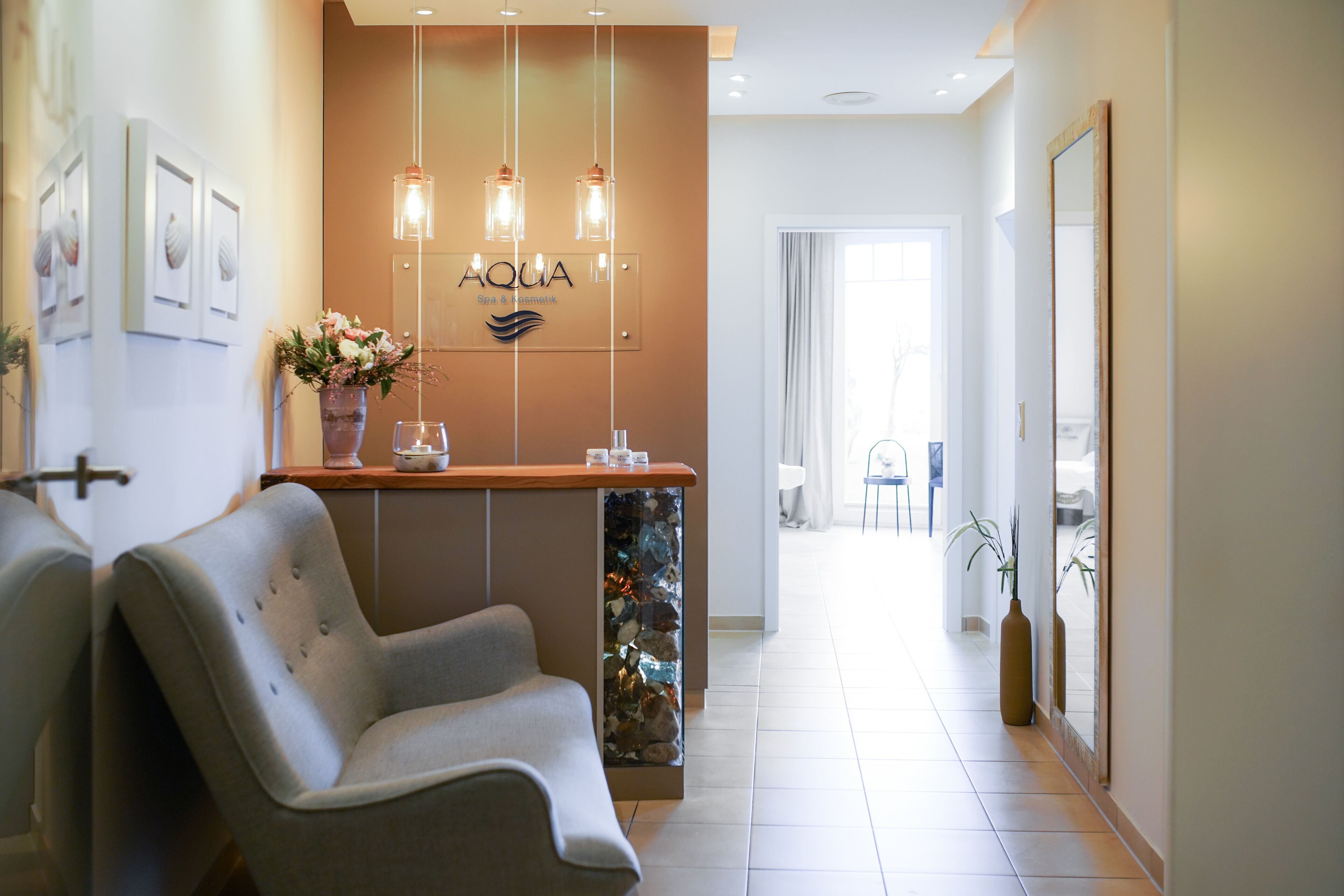 A reception area with a reception desk, a seating area with a chair, a wall-mounted sign reading "AQUIA Spa & Wellness," and a decorative fish tank.