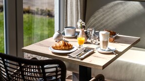 A breakfast table with croissants, orange juice, coffee, and a vase of flowers.