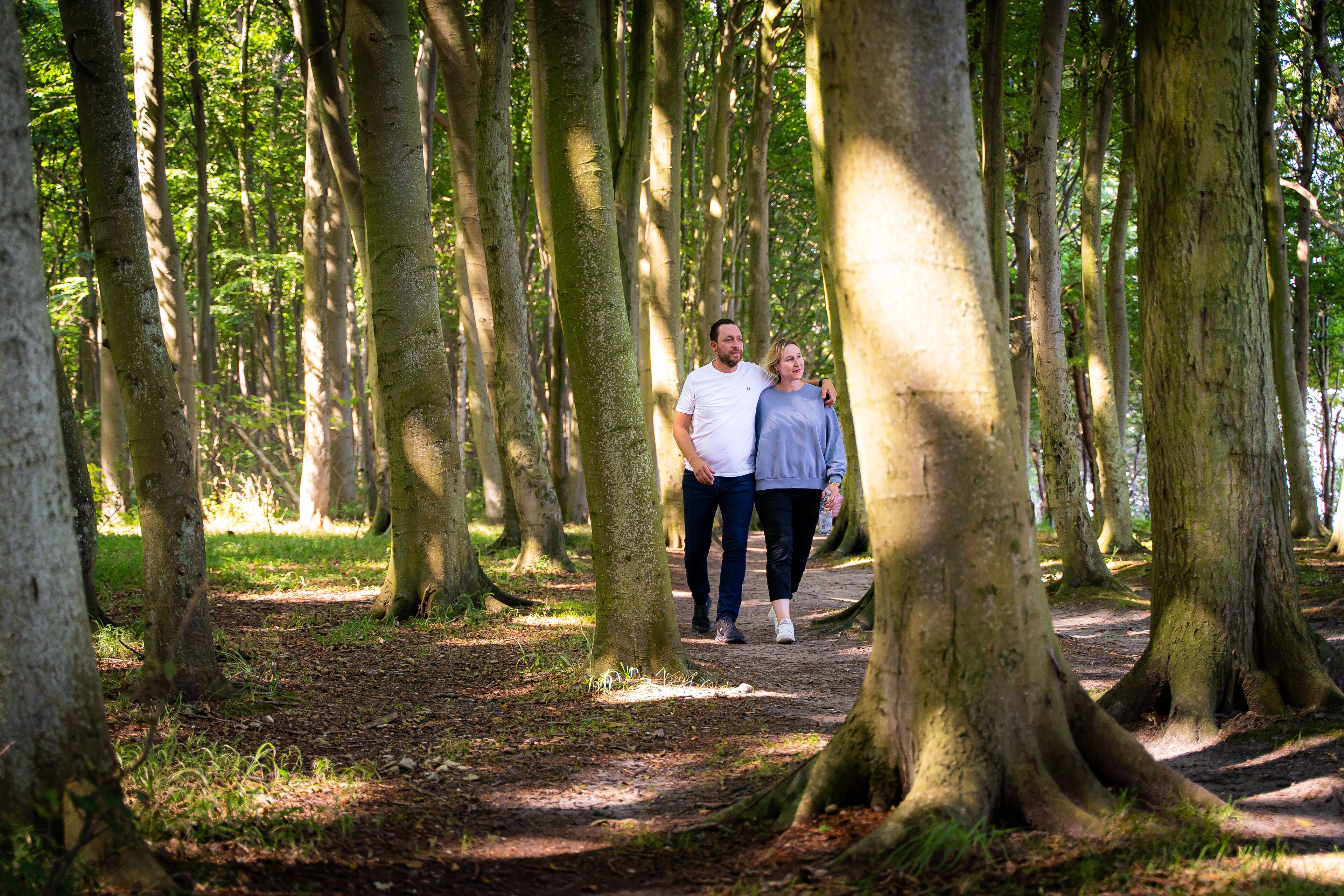 Een stel loopt over een bospad, omringd door hoge bomen.