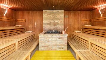 Eine Sauna mit Holzbänken, einem Kamin aus Backsteinen und einer gelben Schutzmatte.