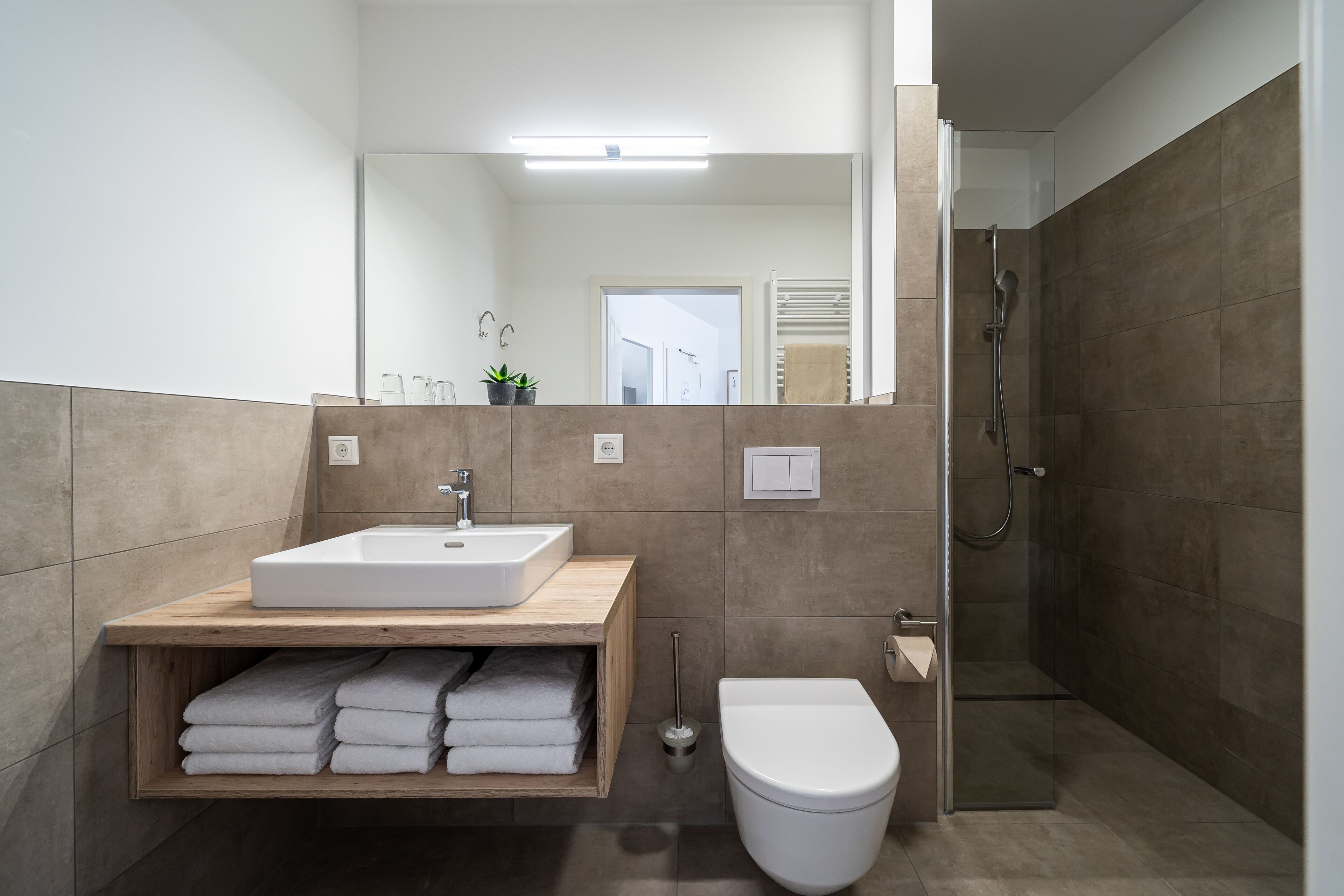 Une salle de bain moderne avec un meuble-lavabo en bois, un lavabo blanc et une cabine de douche en verre.