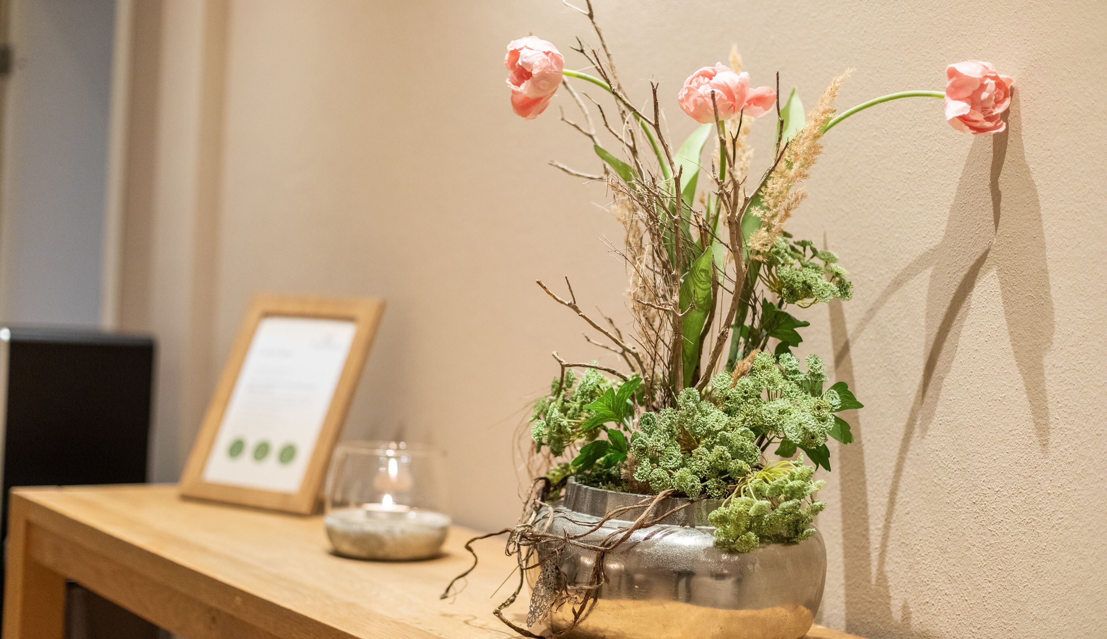 A vase with pink flowers and green foliage on a wooden table.