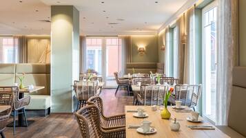 Un restaurant moderne avec des meubles en osier, de grandes fenêtres et un coin salon accueillant.