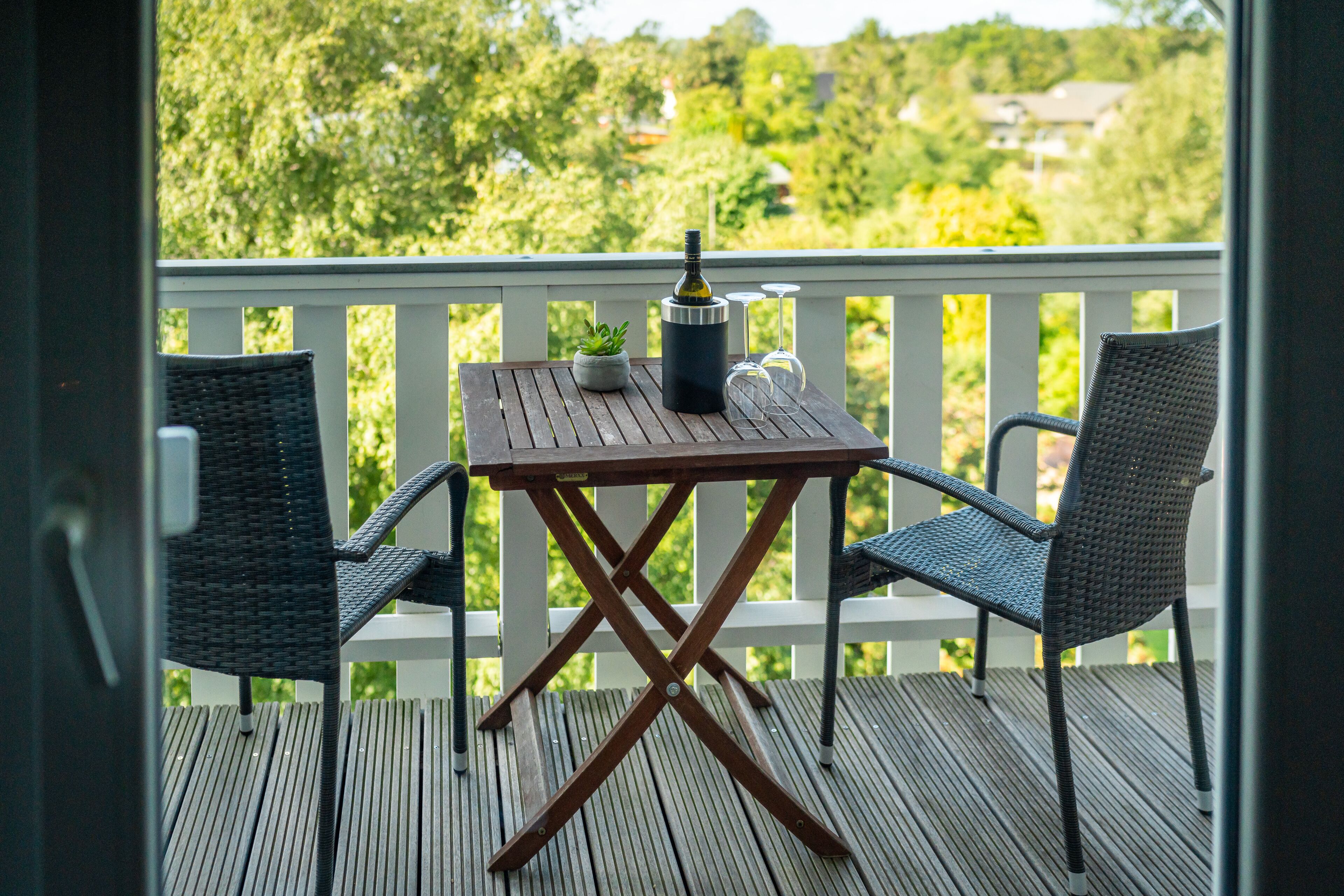 Eine Holzterrasse mit Tisch und zwei Stühlen, einer Flasche und einem Weinglas.