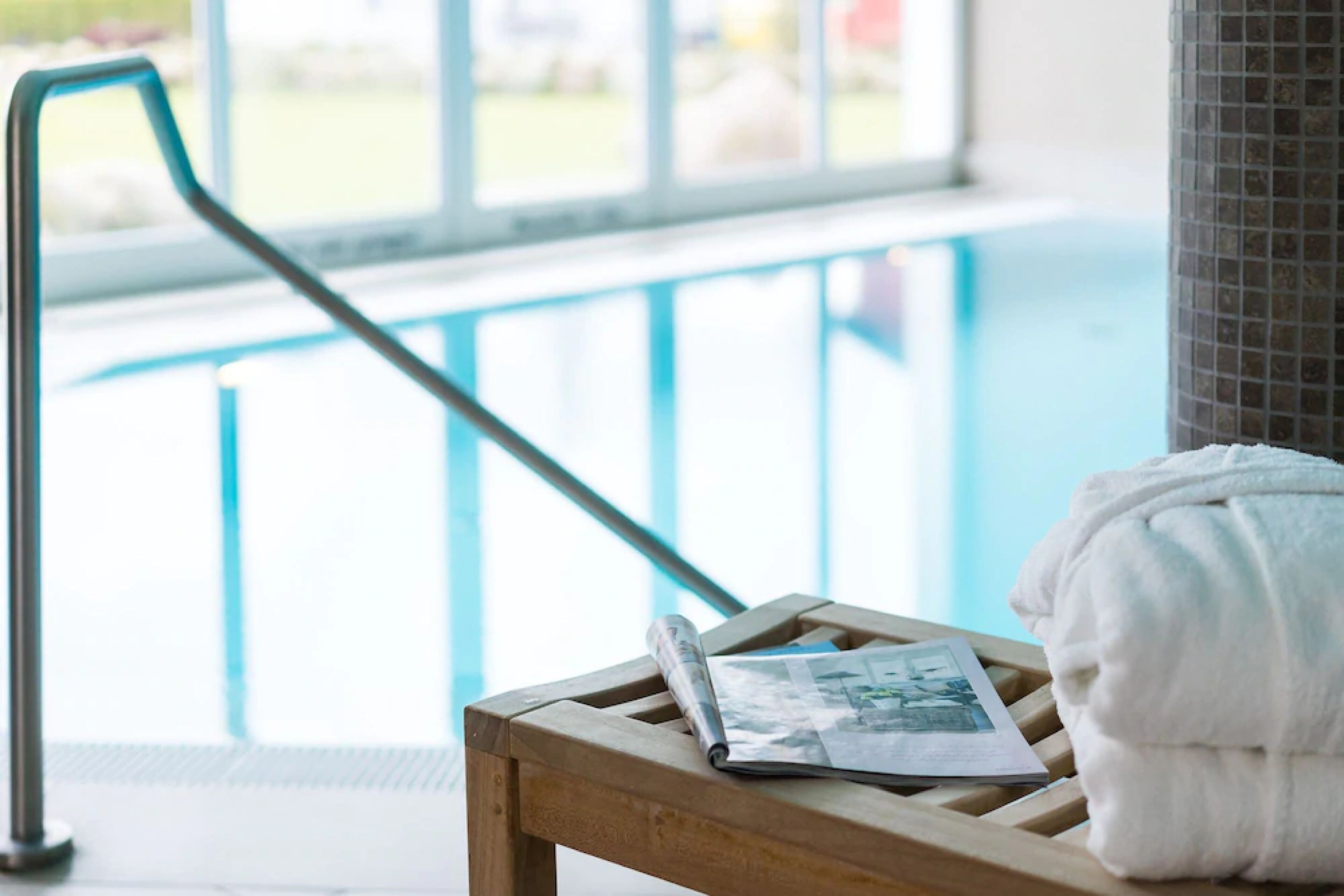 A wooden bench with a towel and a magazine by a poolside.