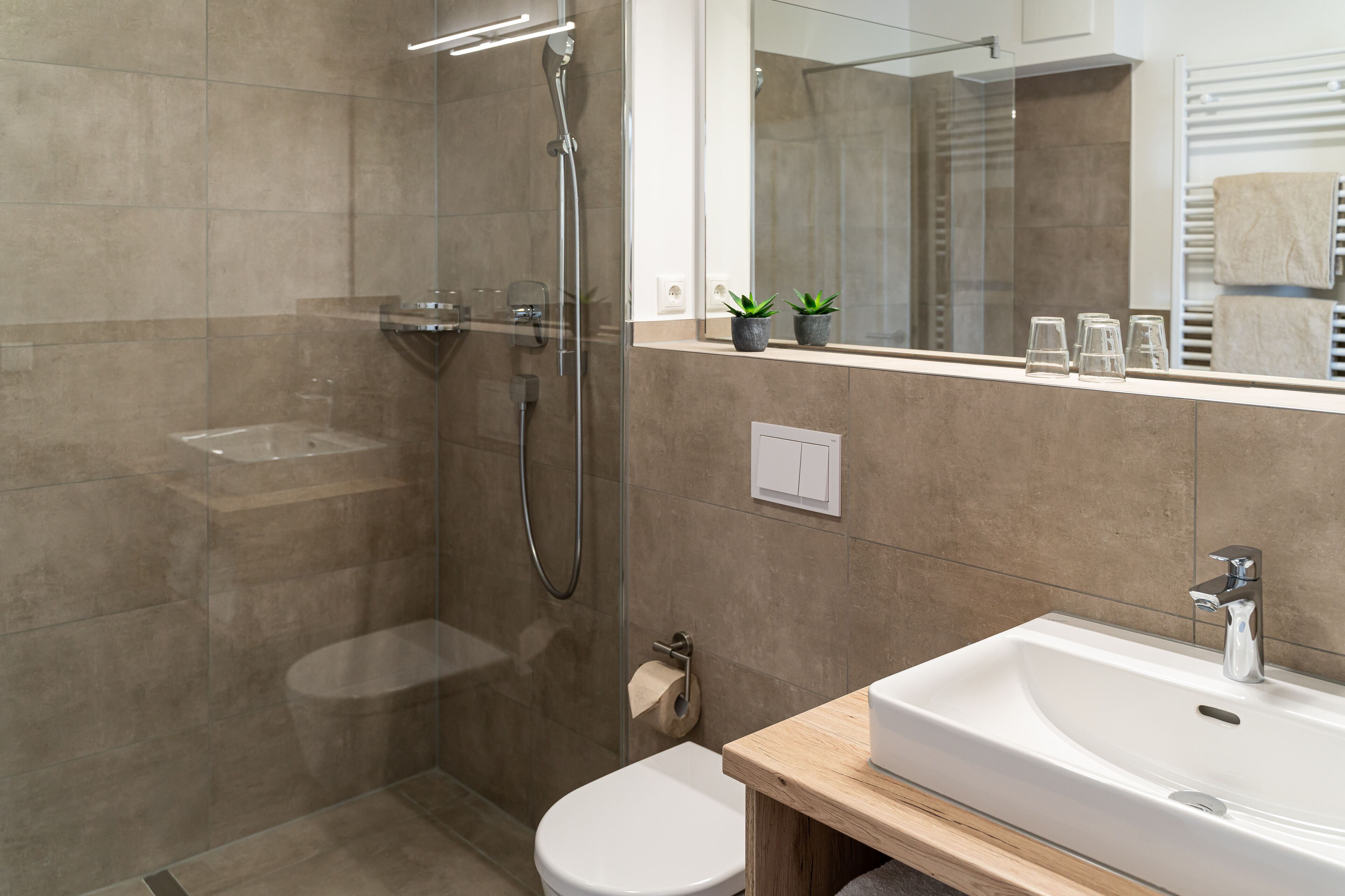 Un baño moderno con ducha de vidrio, un lavamanos blanco y un espejo sobre el lavamanos.