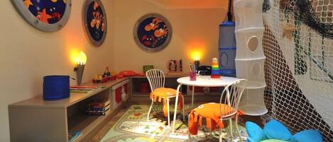 A child's playroom with a climbing net, two round wall decorations, a table with chairs, and a colorful rug.