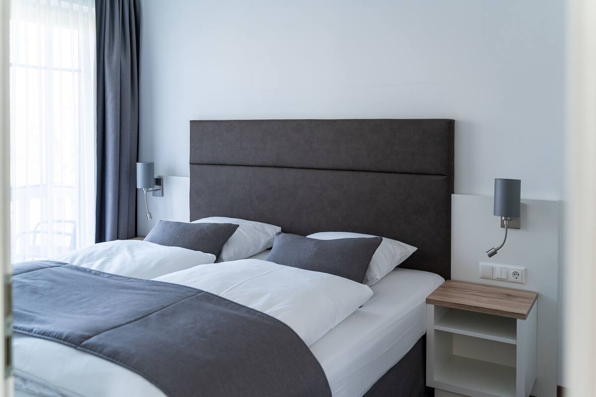 A modern bedroom with a large bed, grey bedding, and a bedside table with a lamp.