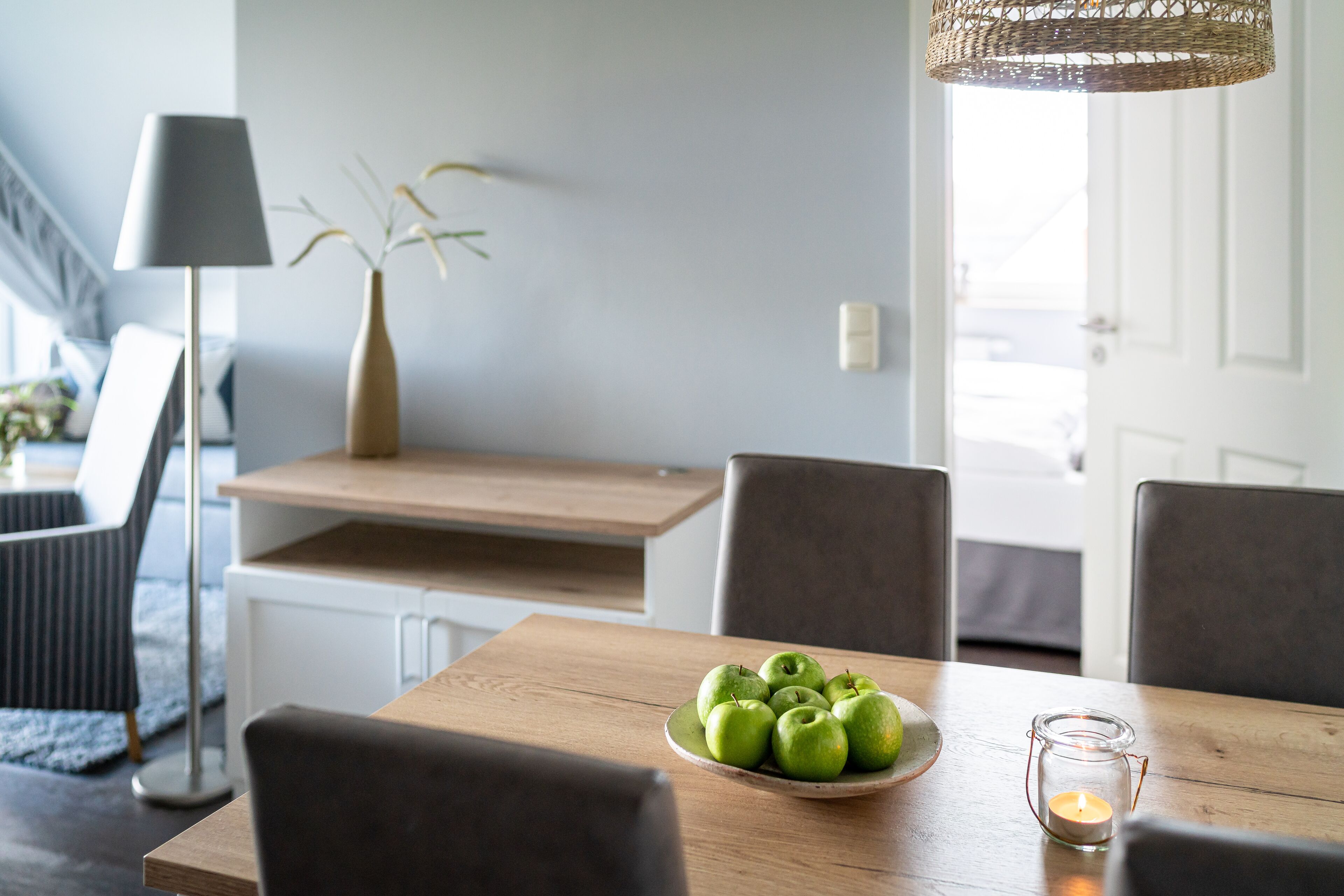 Un comedor con una mesa de madera, un tazón de manzanas verdes, una vela y un florero con plantas.