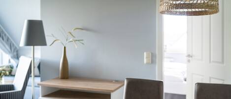 Un coin repas avec une table en bois, un saladier de pommes vertes, une bougie et un vase avec des plantes.