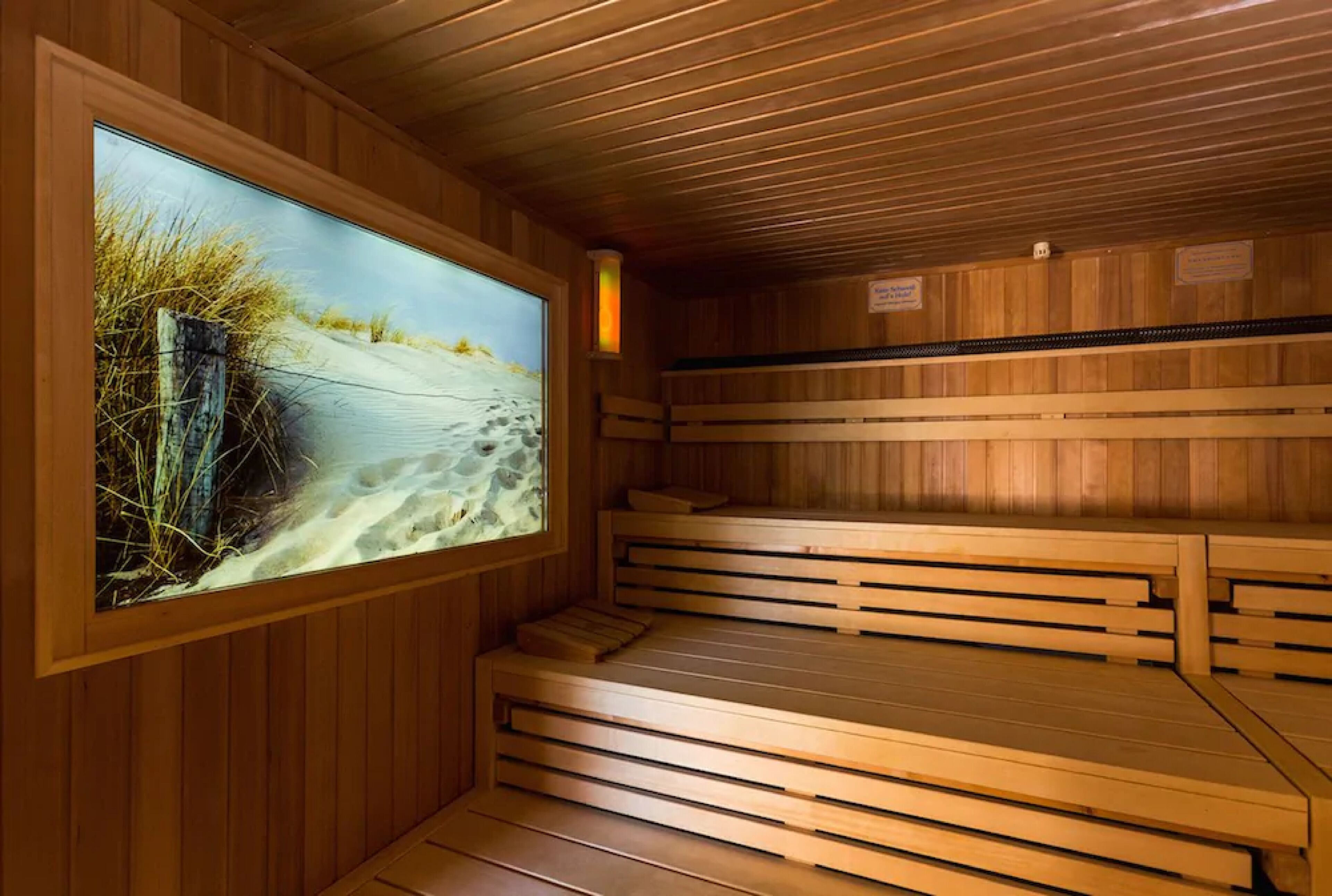 Eine Sauna mit Holzbänken und einem großen Fenster, das einen Blick auf den Strand bietet.
