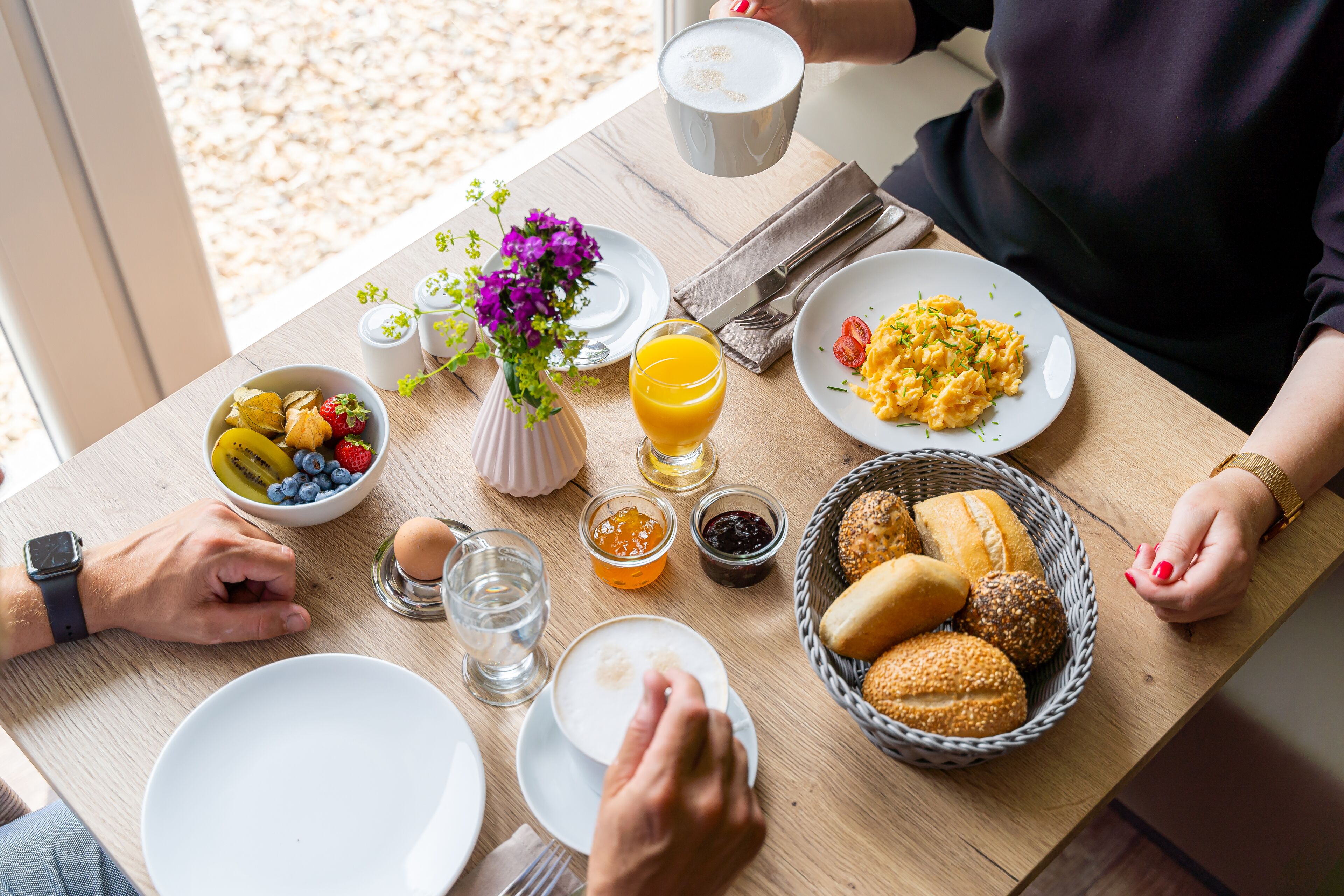 Un desayuno con platos de comida, un cuenco de fruta, un vaso de zumo de naranja y una cesta de pan.