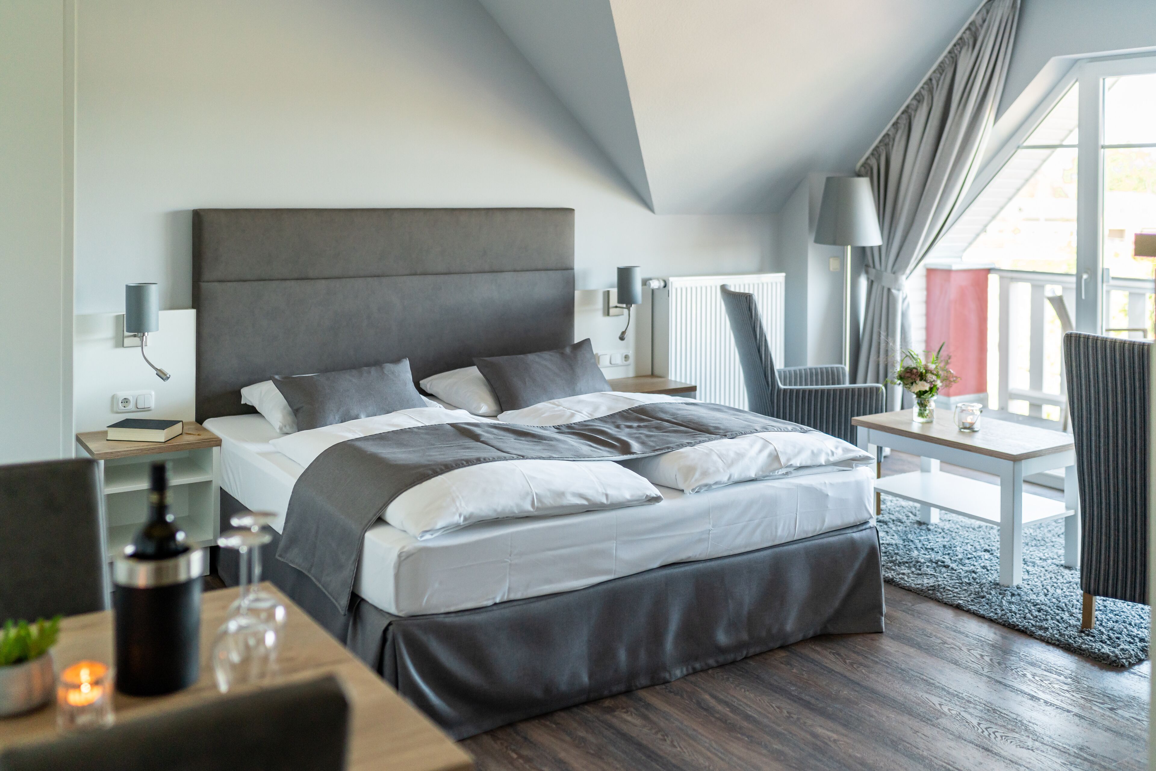 A modern hotel room with a large bed, bedside tables, a small desk, and a view of the outdoors.