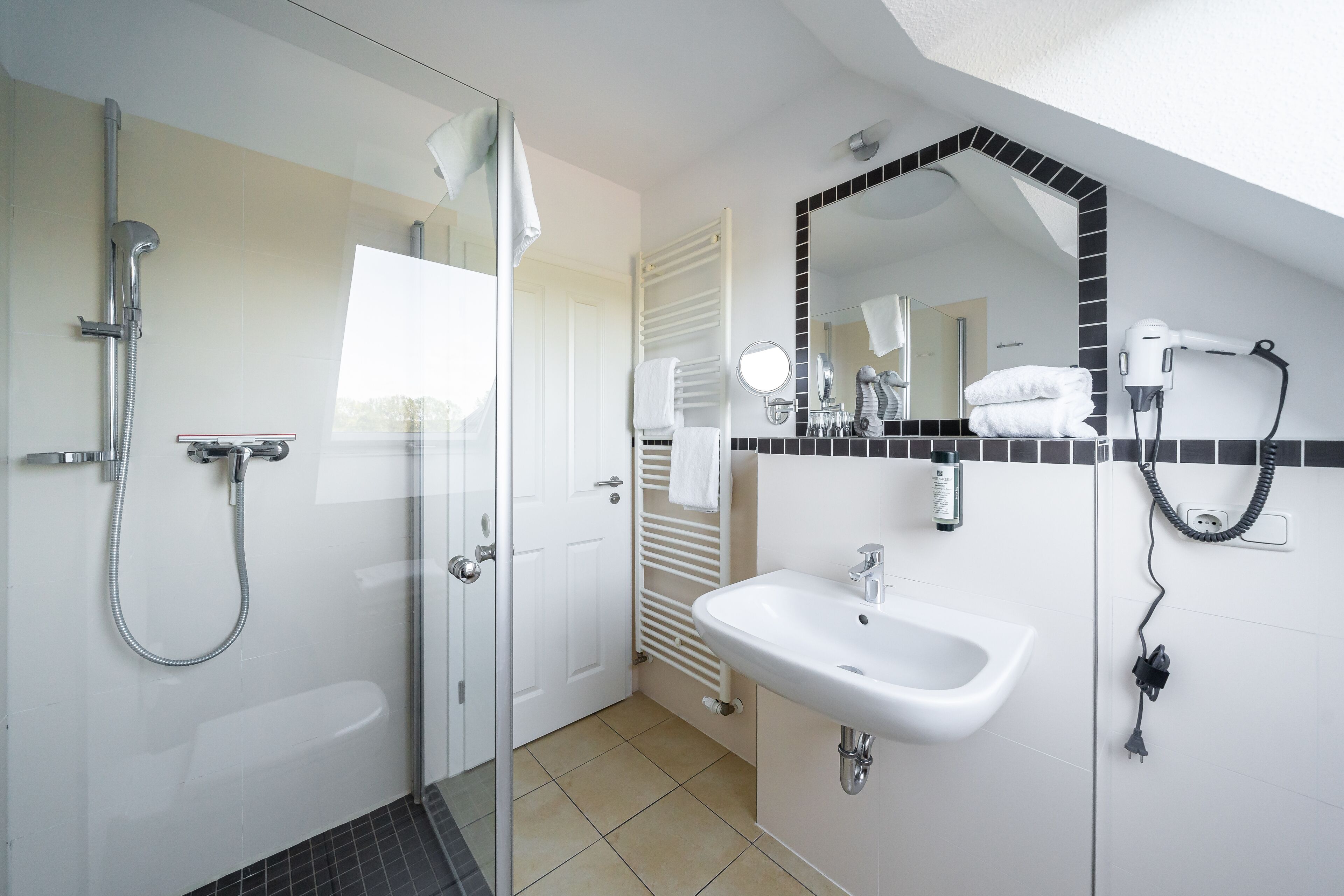 Un baño moderno con cabina de ducha de vidrio, un lavabo blanco y un espejo grande con marco negro.