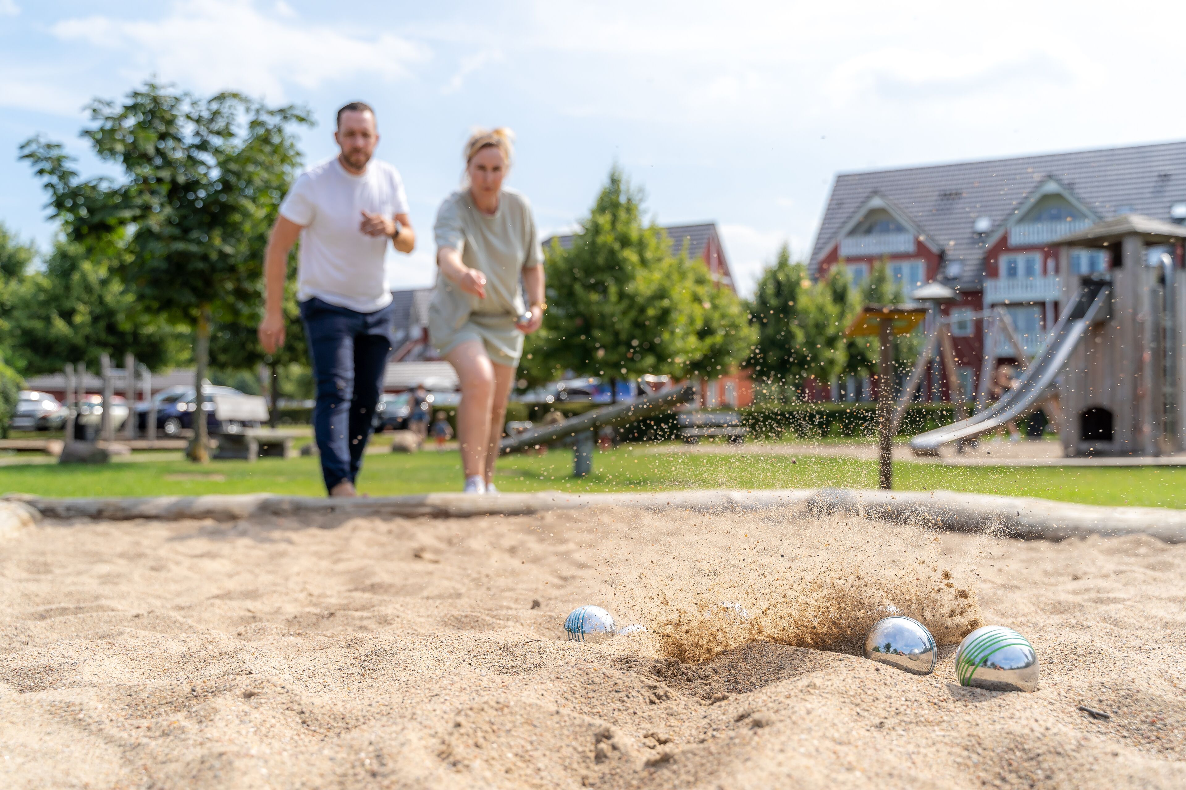 Ein Sandkasten mit drei Bällen und einem Spielplatz im Hintergrund.