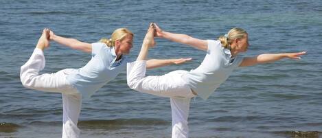 Two individuals performing a yoga pose on a beach with the ocean in the background.