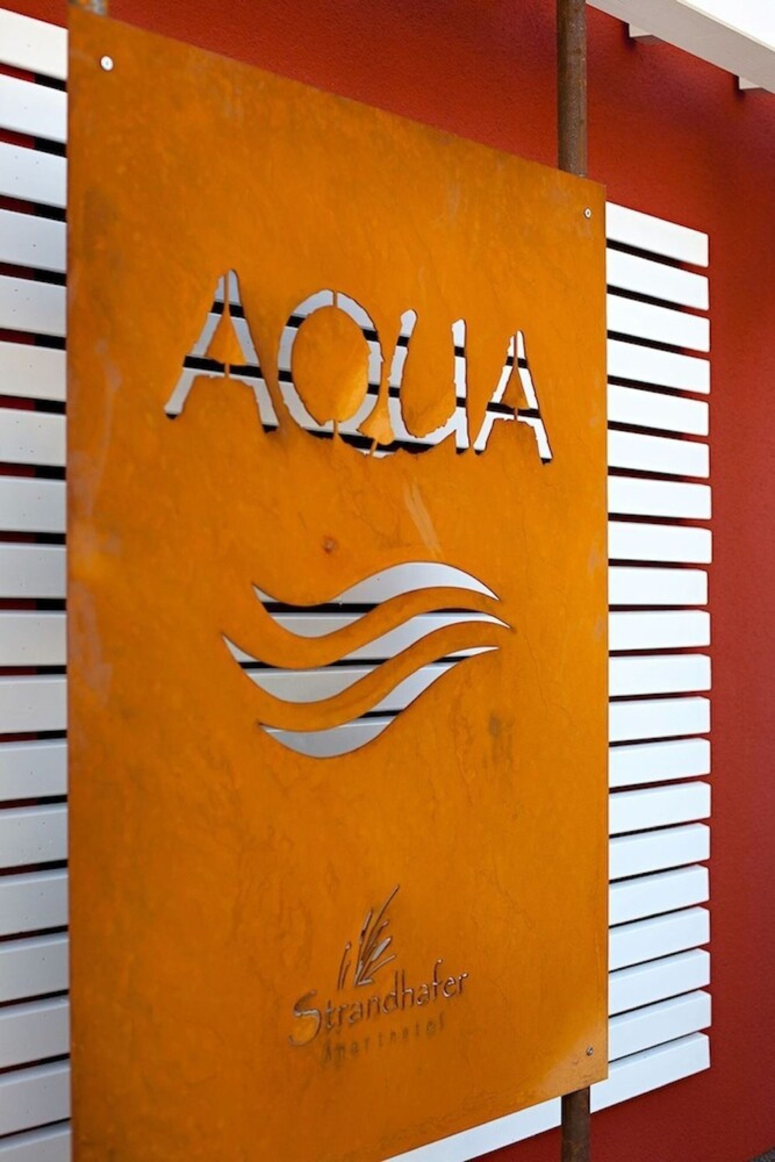 Señal con la palabra 'AQUA' y un diseño de ola, indicando un servicio o instalación relacionado con el agua.
