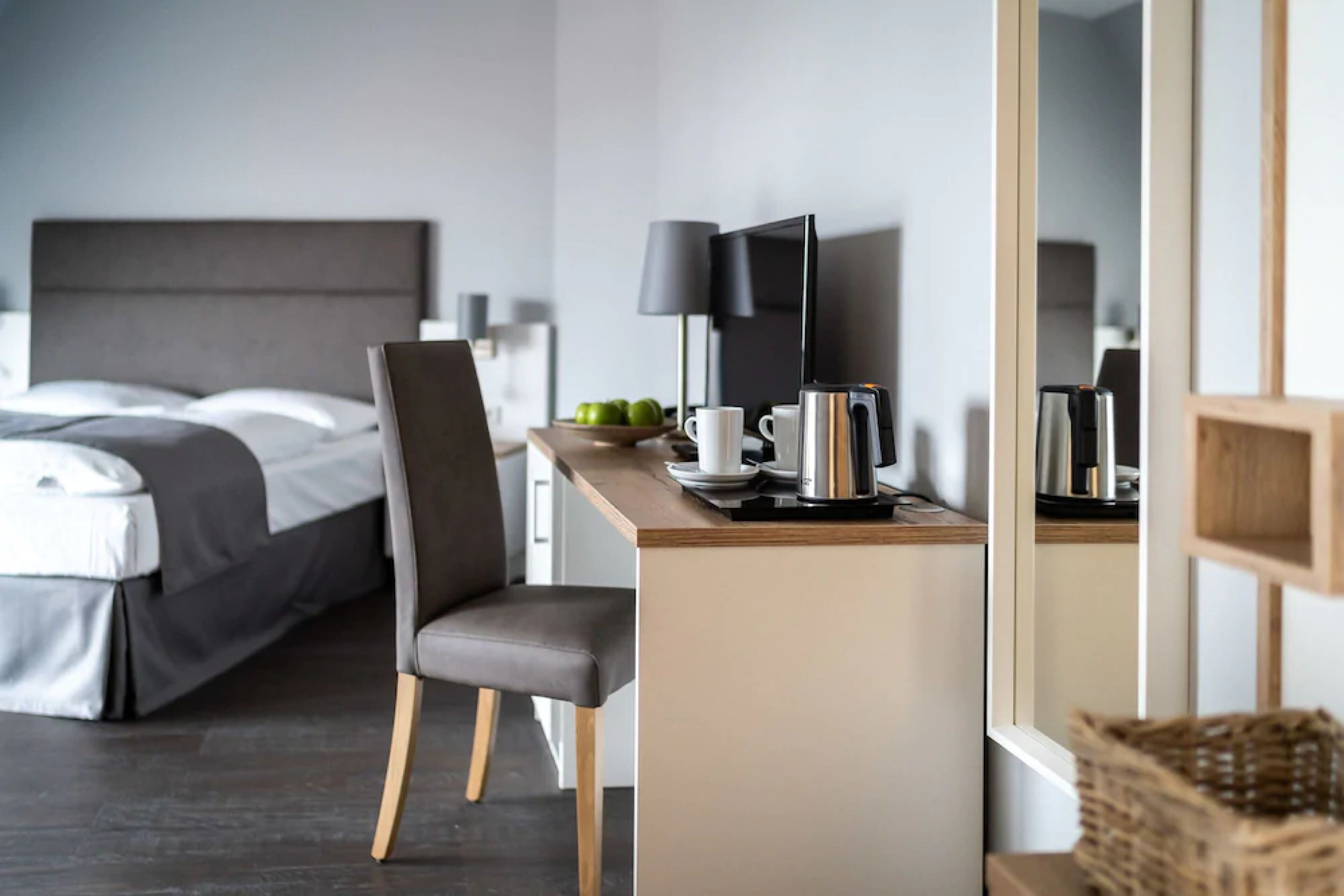 A modern hotel room with a bed, a desk with a laptop, a coffee maker, and a TV.