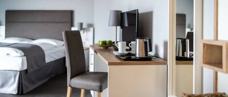A modern hotel room with a bed, a desk with a laptop, a coffee maker, and a TV.