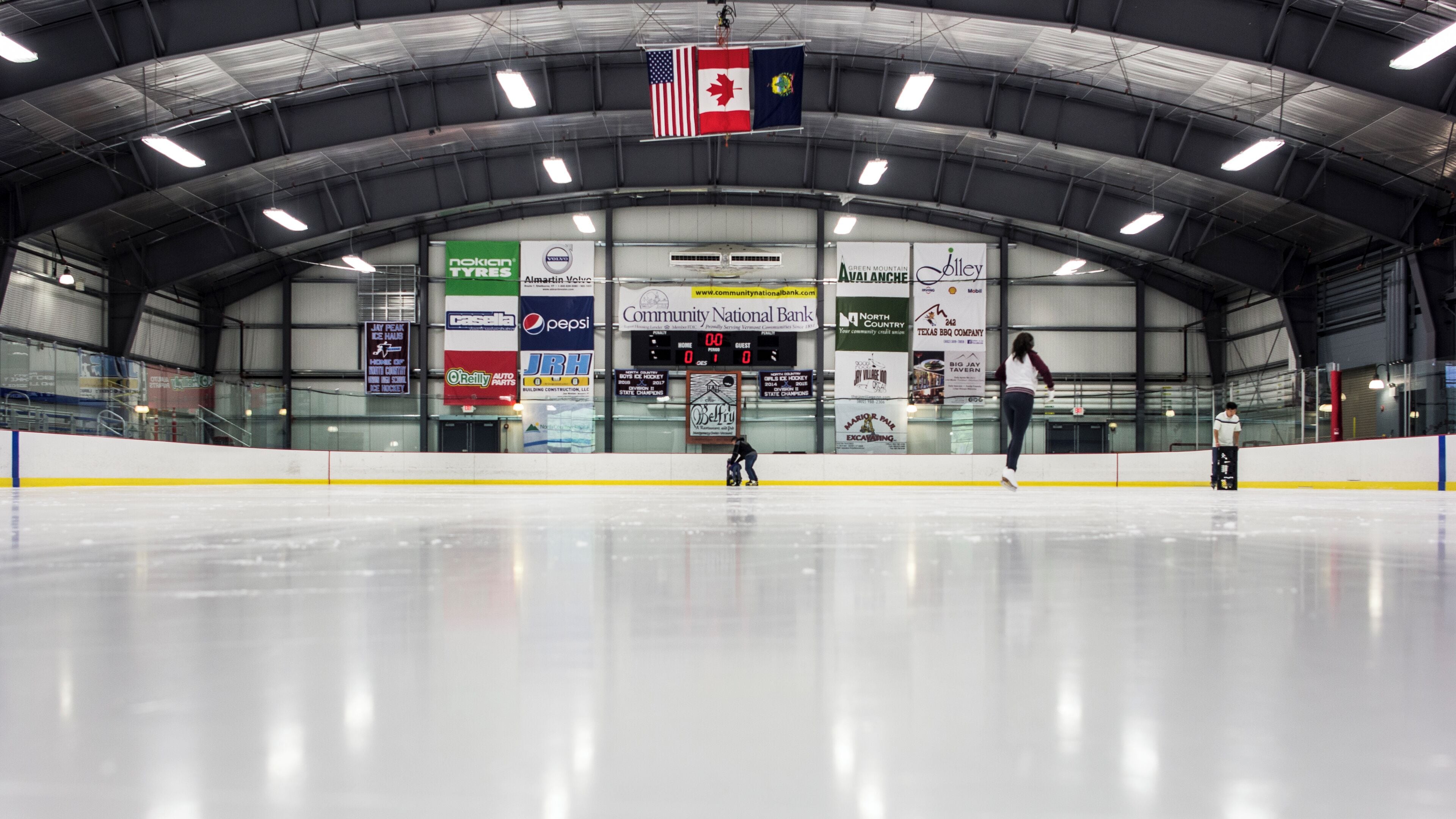 An indoor ice rink with banners advertising various brands and a scoreboard.