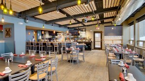A restaurant with multiple dining tables and chairs, a bar area, and a television screen. - Jay Peak Resort (North Troy)