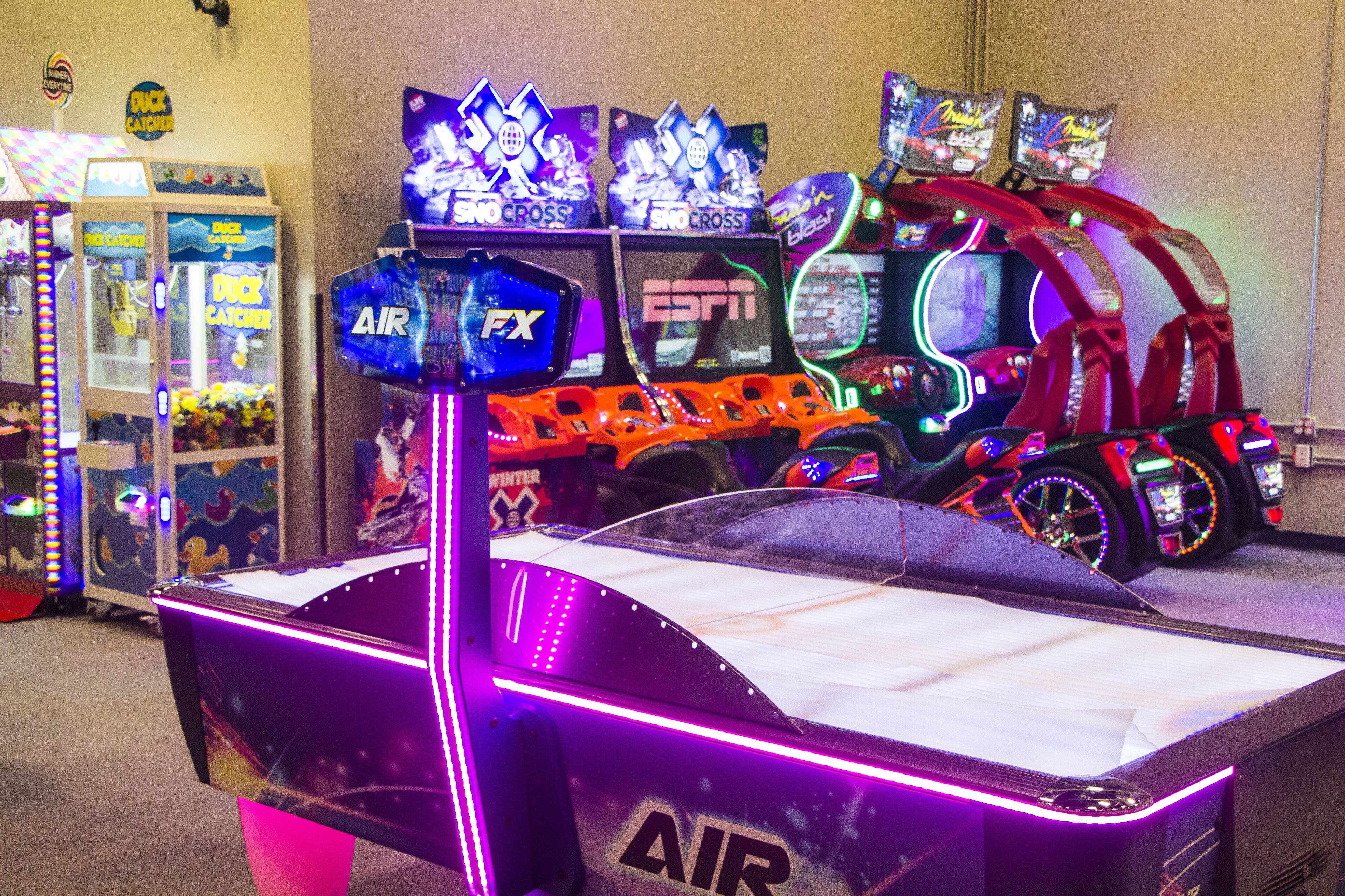 A row of arcade machines, including 'Duck Catcher' and 'Sno Cross' games, with neon lights and a 'FX' machine in the foreground.