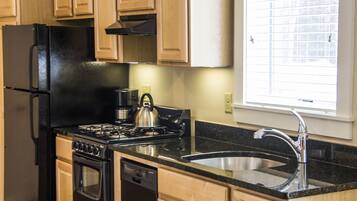 A kitchen with wooden cabinets, a black refrigerator, a stove, a kettle, and a sink.