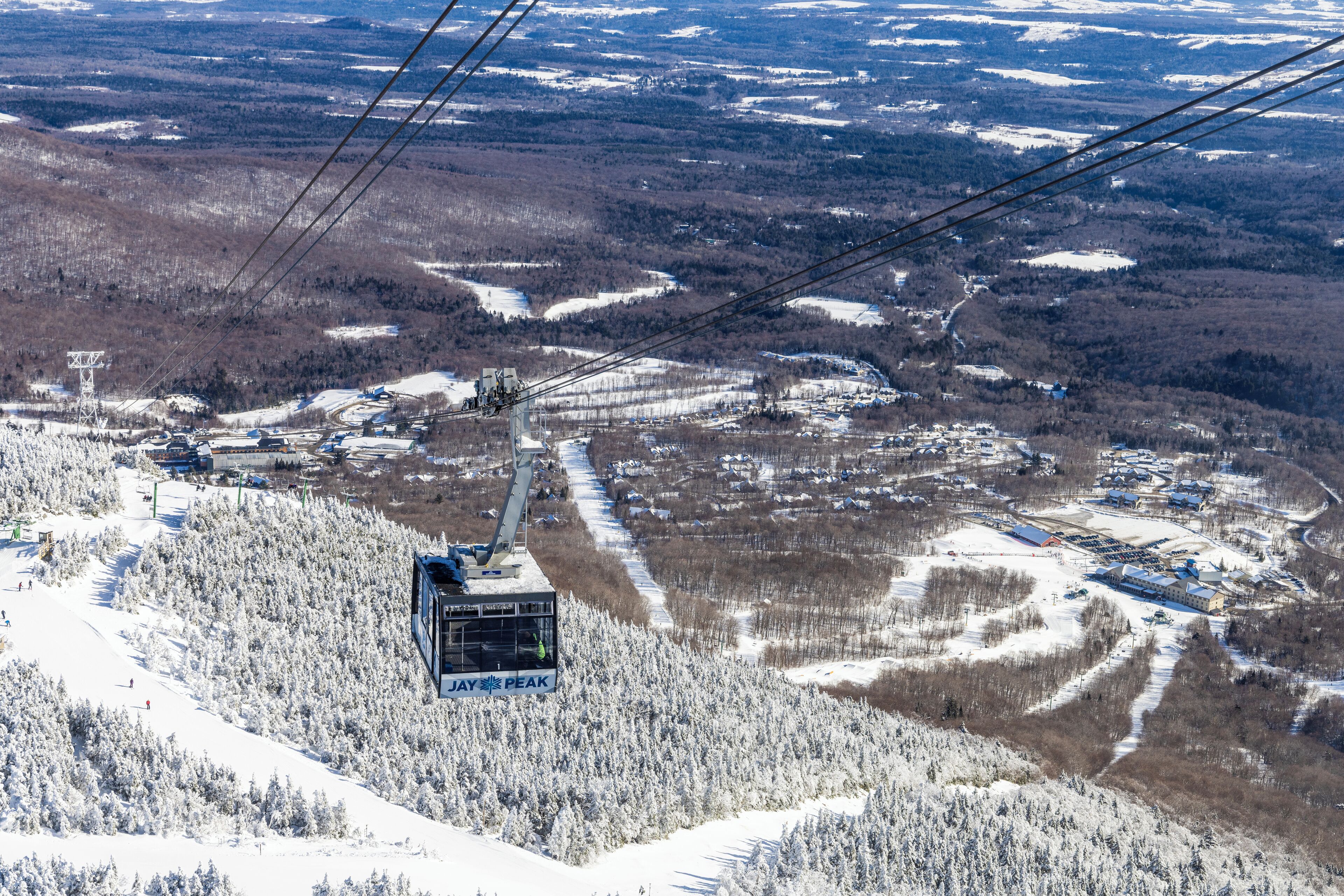 A cable car system with a chairlift moving over a snowy landscape, surrounded by trees and buildings.