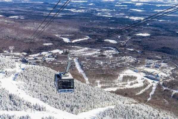 A cable car system with a chairlift moving over a snowy landscape, surrounded by trees and buildings.