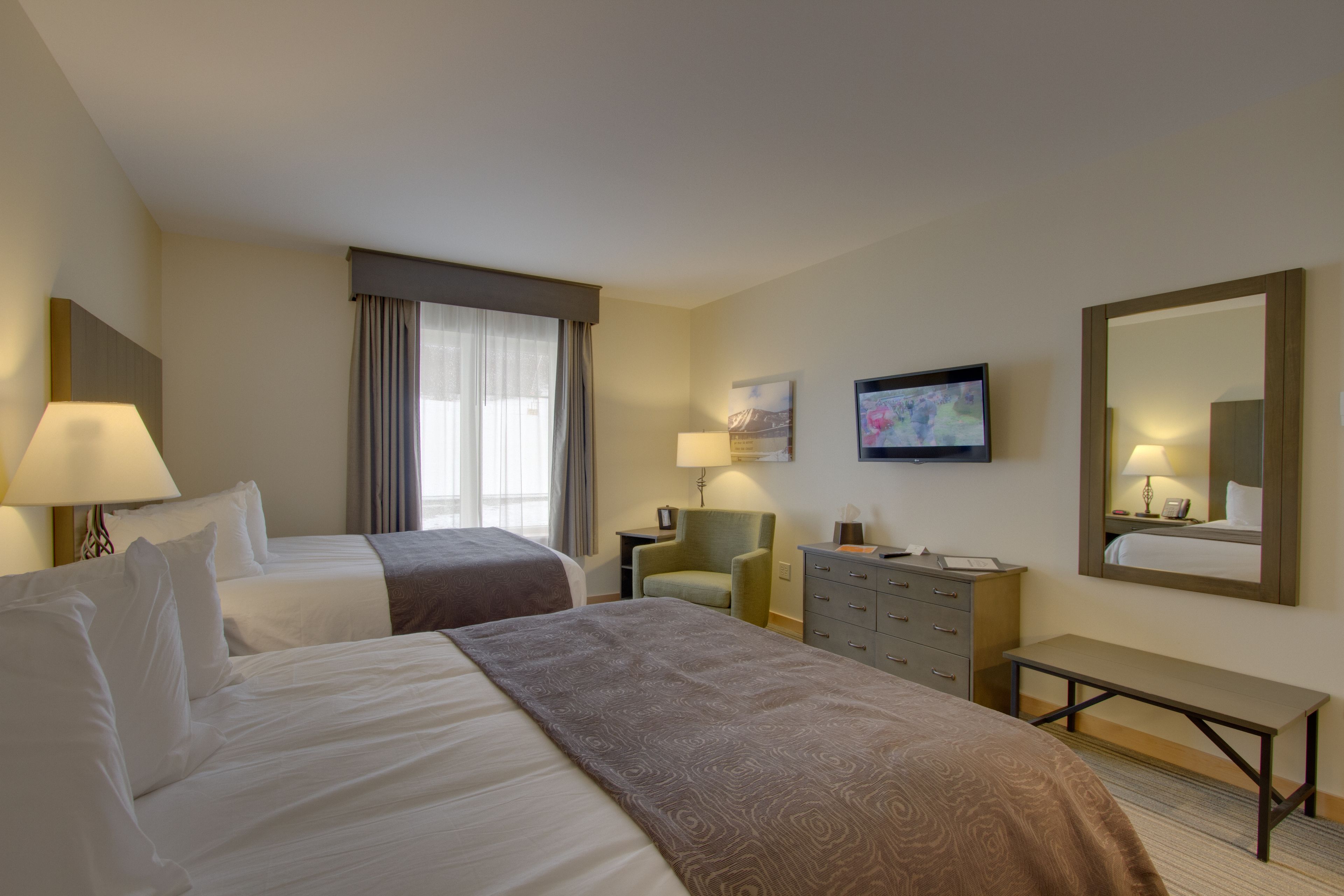 A hotel room with two beds, a desk, a chair, a dresser, and a TV.
