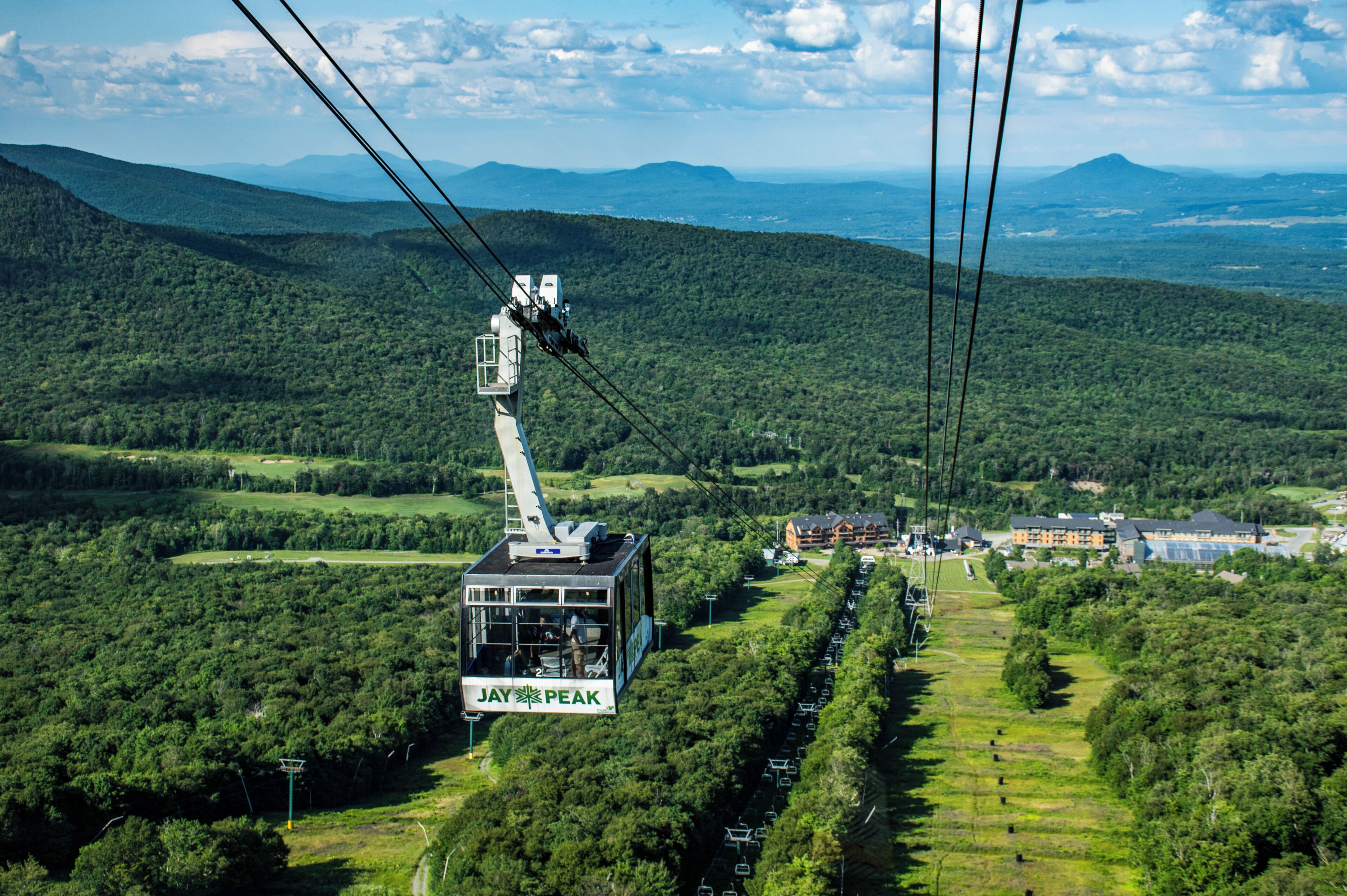 A cable car labeled "Jay Peak" suspended over a forested landscape with distant mountains.