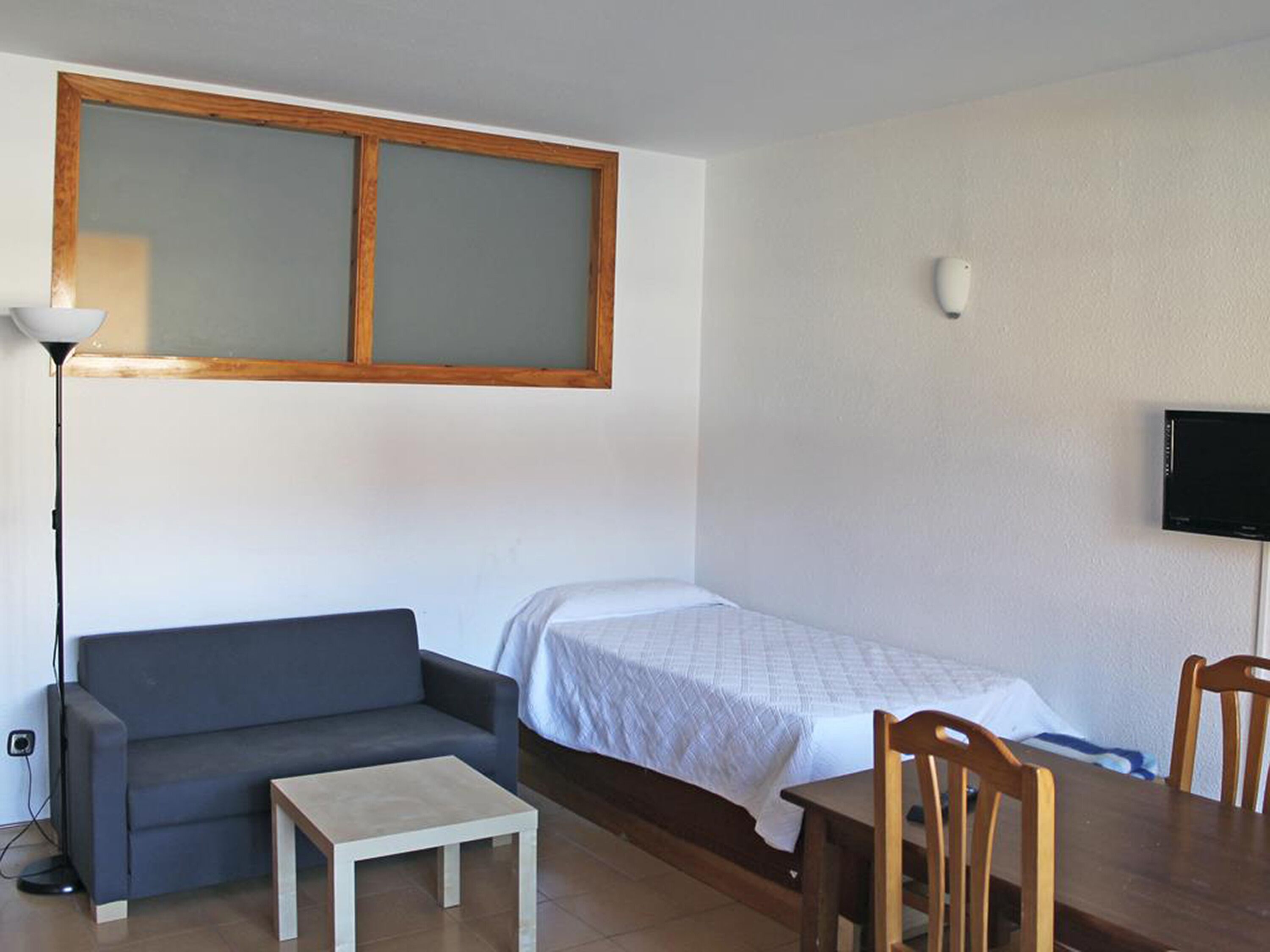 Una habitación pequeña y sencilla con cama, sofá, mesa y televisión.