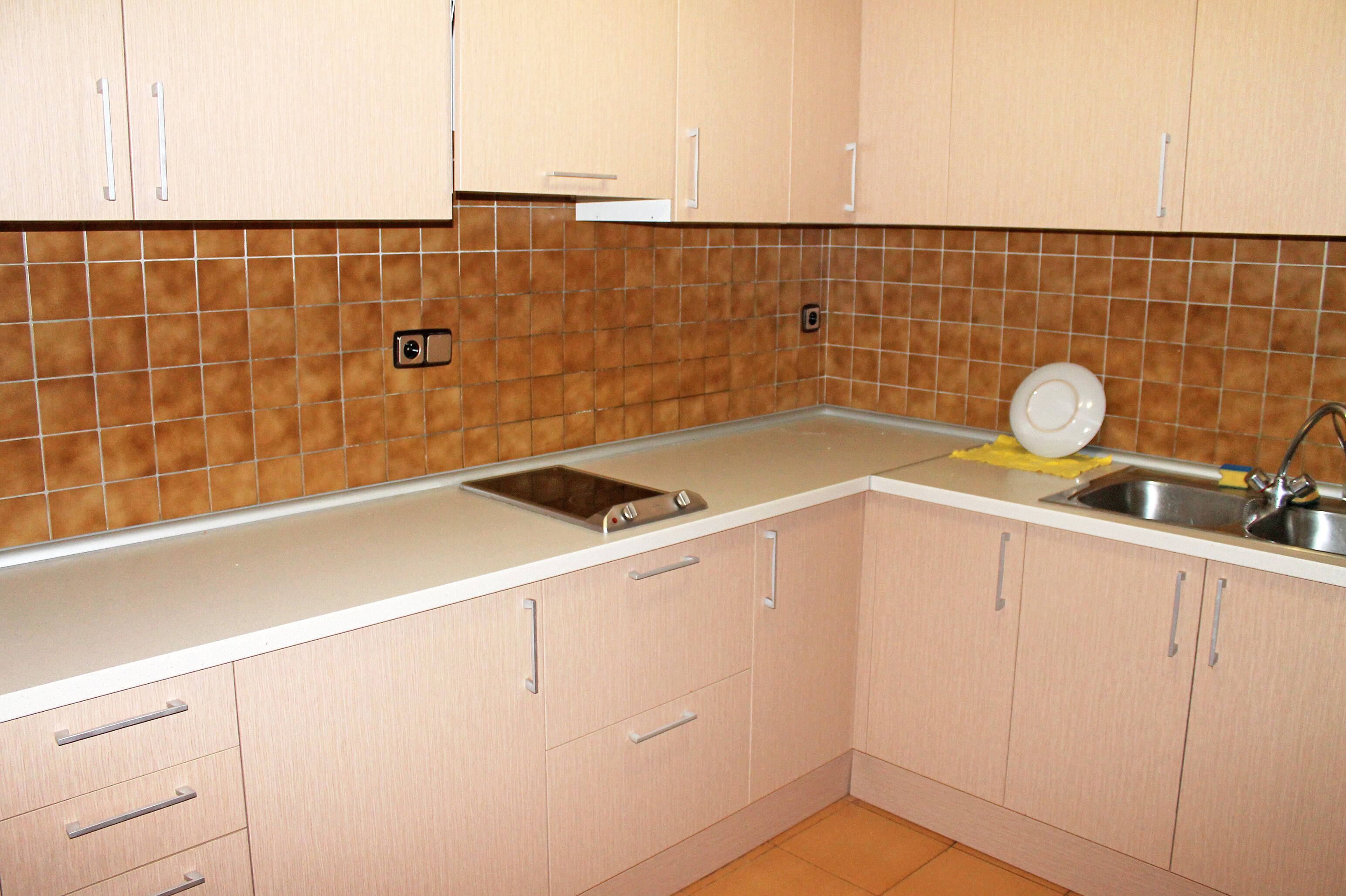 Una cocina con armarios de colores claros, un lavamanos de acero inoxidable y un salpicadero azulejado.
