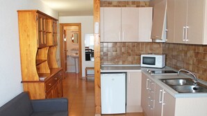 Cocina compacta con microondas, pileta y heladera pequeña. En la zona de estar, hay un mueble de madera y un sofá gris.