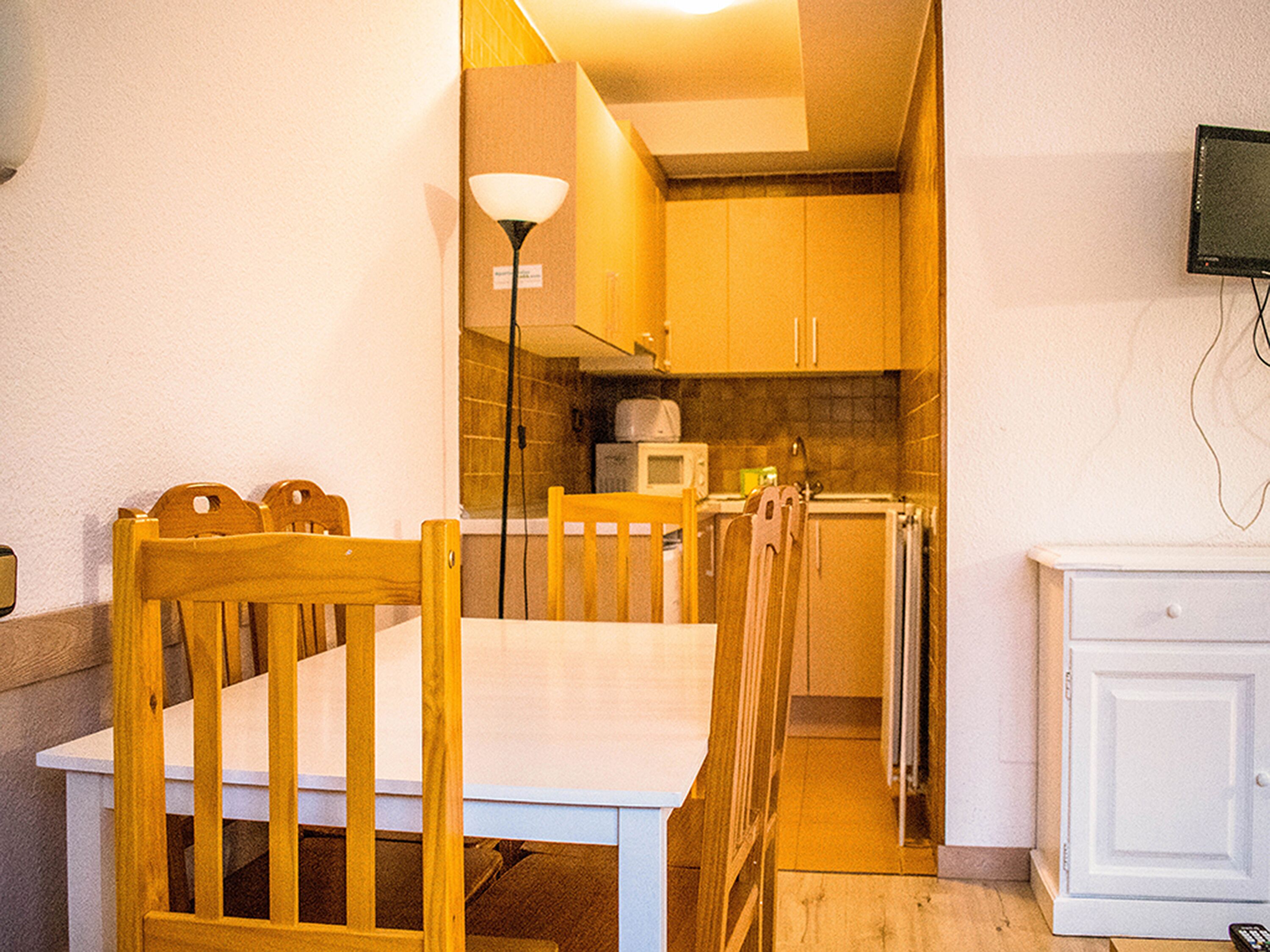 A compact kitchen with wooden cabinets, a microwave, and a dining table with chairs.