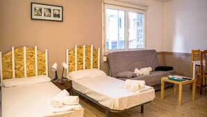 Habitación de hotel con dos camas, un sofá, una mesita y una ventana con vistas a edificios.