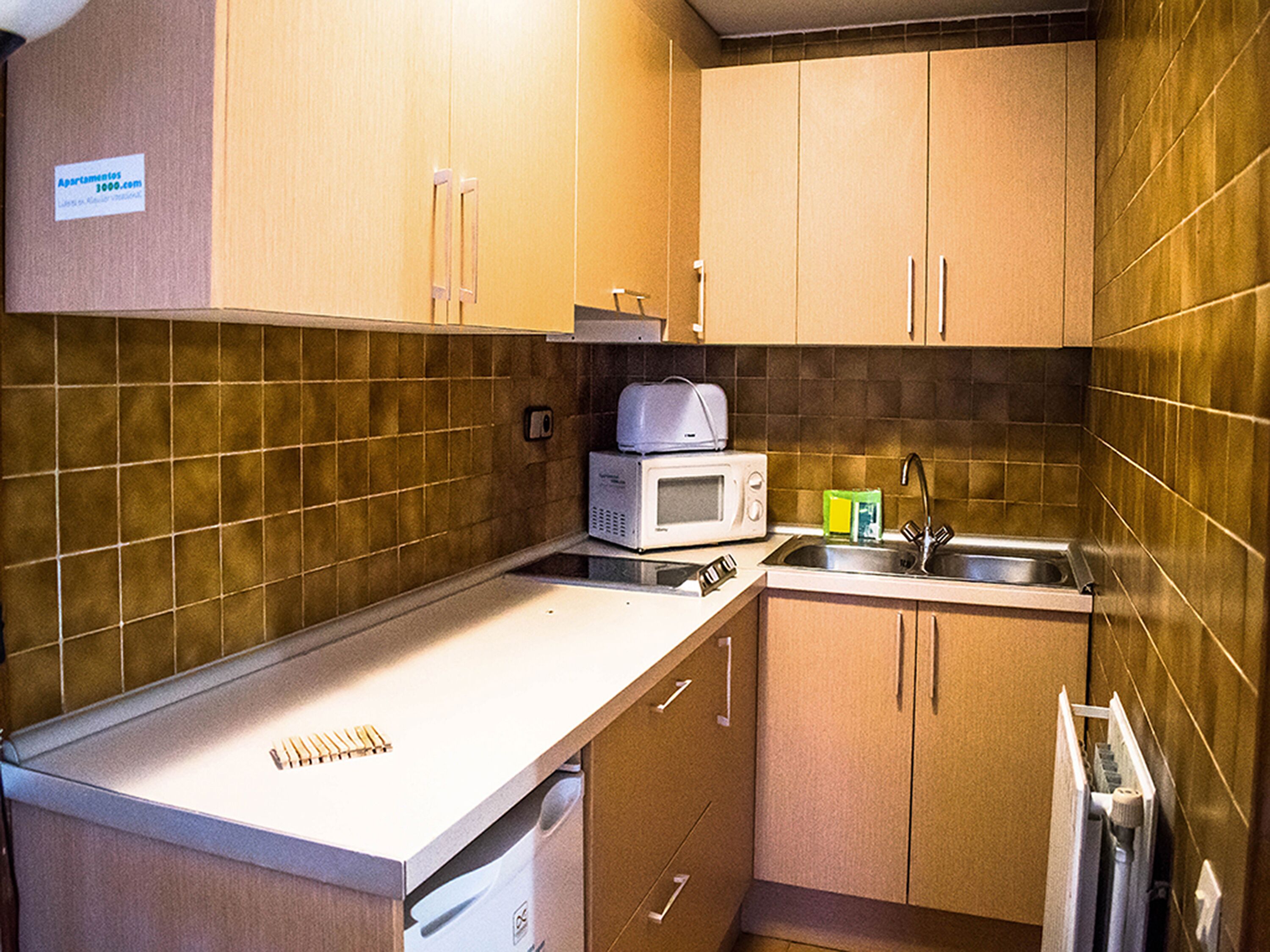 A compact kitchen with wooden cabinets, a microwave, a sink, and a small countertop.