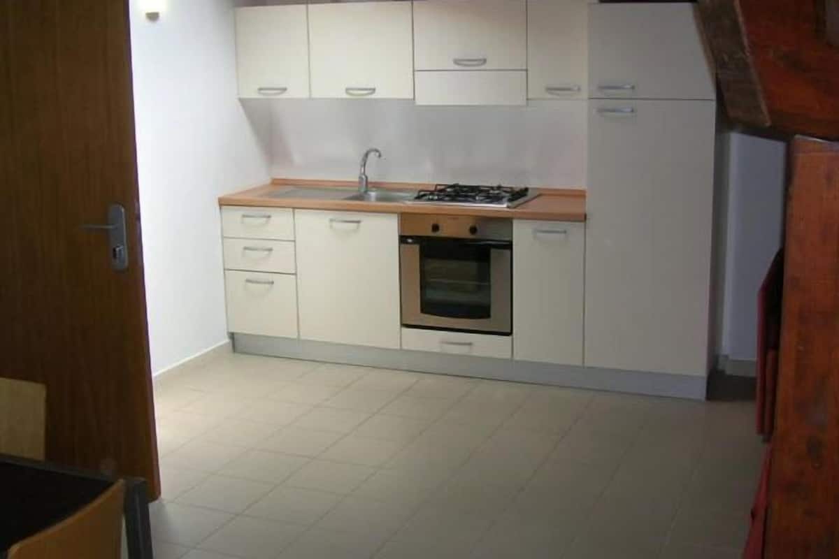 Une cuisine de taille réduite avec des meubles blancs, un plan de travail en bois, un évier, une cuisinière et un four.