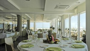 A restaurant with round tables set for dining, large windows offering a view of the ocean, and a modern interior design. - Casa del Mar (Roseto degli Abruzzi)